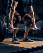 Genouillères de compression noir et cuivre portées aux deux genoux pendant un soulevé de barre en salle de musculation